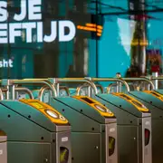 Hilera de barreras de acceso con lectores amarillos para tarjeta en una estación de metro de Ámsterdam, con carteles en neerlandés al fondo
