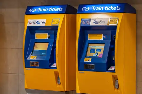 Dos máquinas expendedoras de billetes de NS, amarillas y azules, que indican que aceptan solo tarjeta de débito o crédito