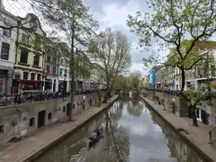 Canal de Utrecht flanqueado por casas de ladrillo y árboles, con bicicletas aparcadas a lo largo del muelle y una barca en el agua