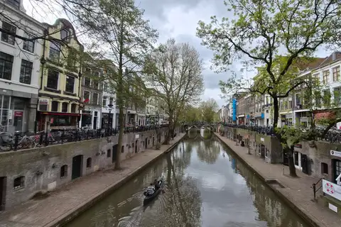 Canal de Utrecht flanqueado por casas de ladrillo y árboles, con bicicletas aparcadas a lo largo del muelle y una barca en el agua