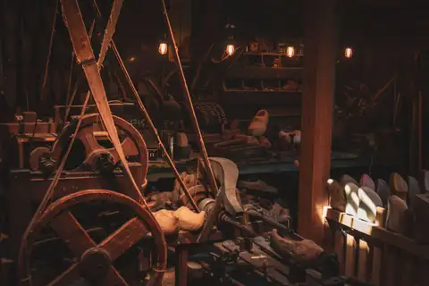 Interior penumbroso de un taller tradicional de zuecos, con maquinaria de madera, poleas, herramientas y zuecos sin pintar