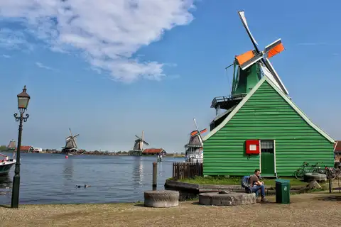 Molinos de viento de madera junto al río Zaan en Zaanse Schans, con una casa verde en primer plano y un farol