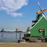 Molinos de viento de madera junto al río Zaan en Zaanse Schans, con una casa verde en primer plano y un farol