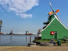 Molinos de viento de madera junto al río Zaan en Zaanse Schans, con una casa verde en primer plano y un farol