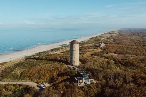 Vista aérea de la playa ancha de Domburg, con la torre de agua histórica entre dunas cubiertas de vegetación y el mar en calma