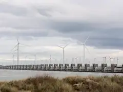 Pilares de hormigón de la barrera del Escalda Oriental sobre el agua, con aerogeneradores detrás, dunas en primer plano y cielo nublado